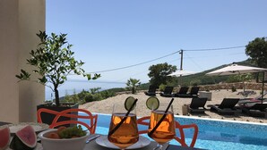 Ett bord vid poolkanten med ett glas apelsindricka, en skål med frukt och en skiva vattenmelon.