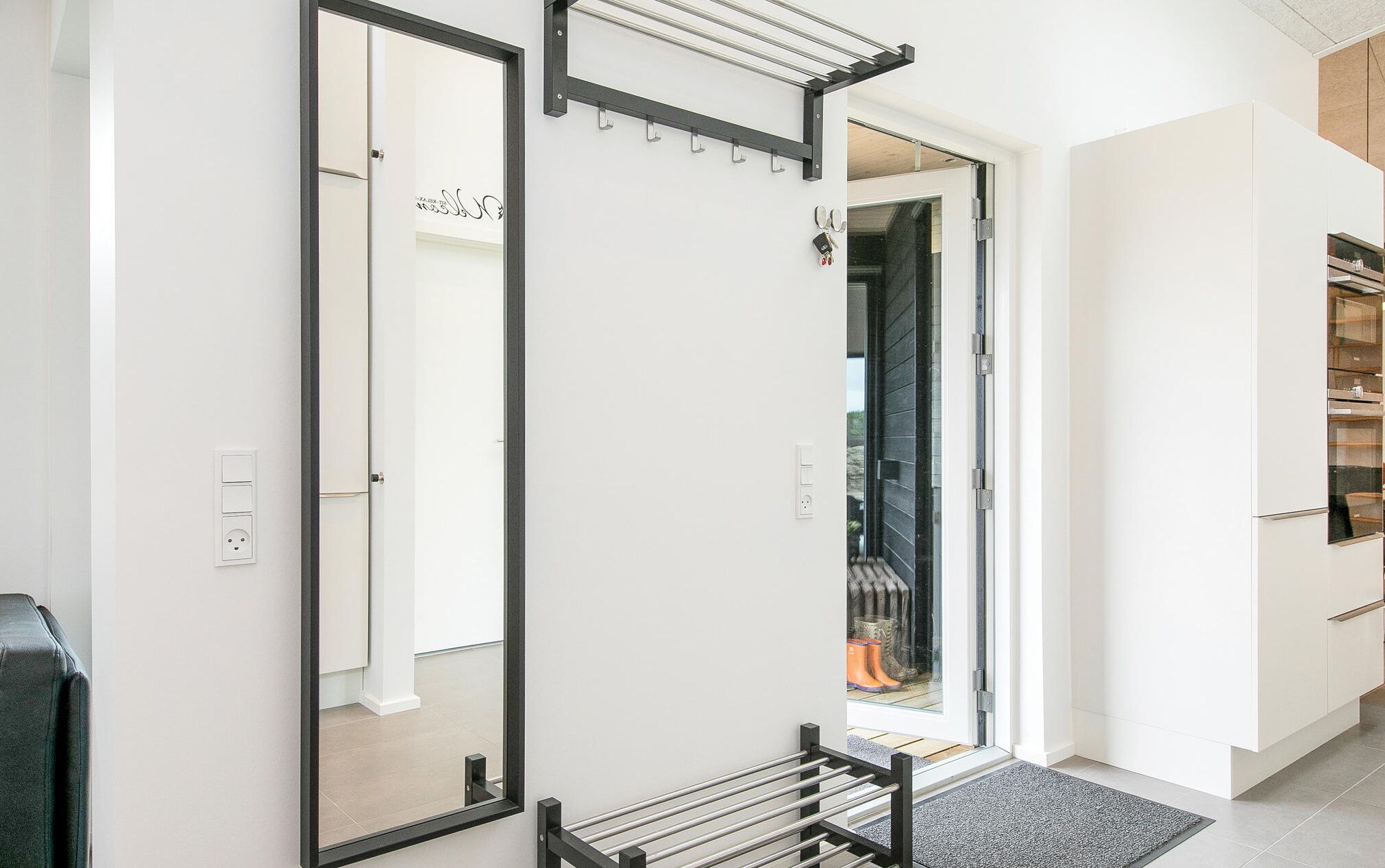 Ein modernes Interieur mit einem Flur, der zu einem Raum mit einer Schiebetür führt. Man sieht einen Kleiderhaken, eine Tür mit Fensterteil und einen eingebauten Backofen.