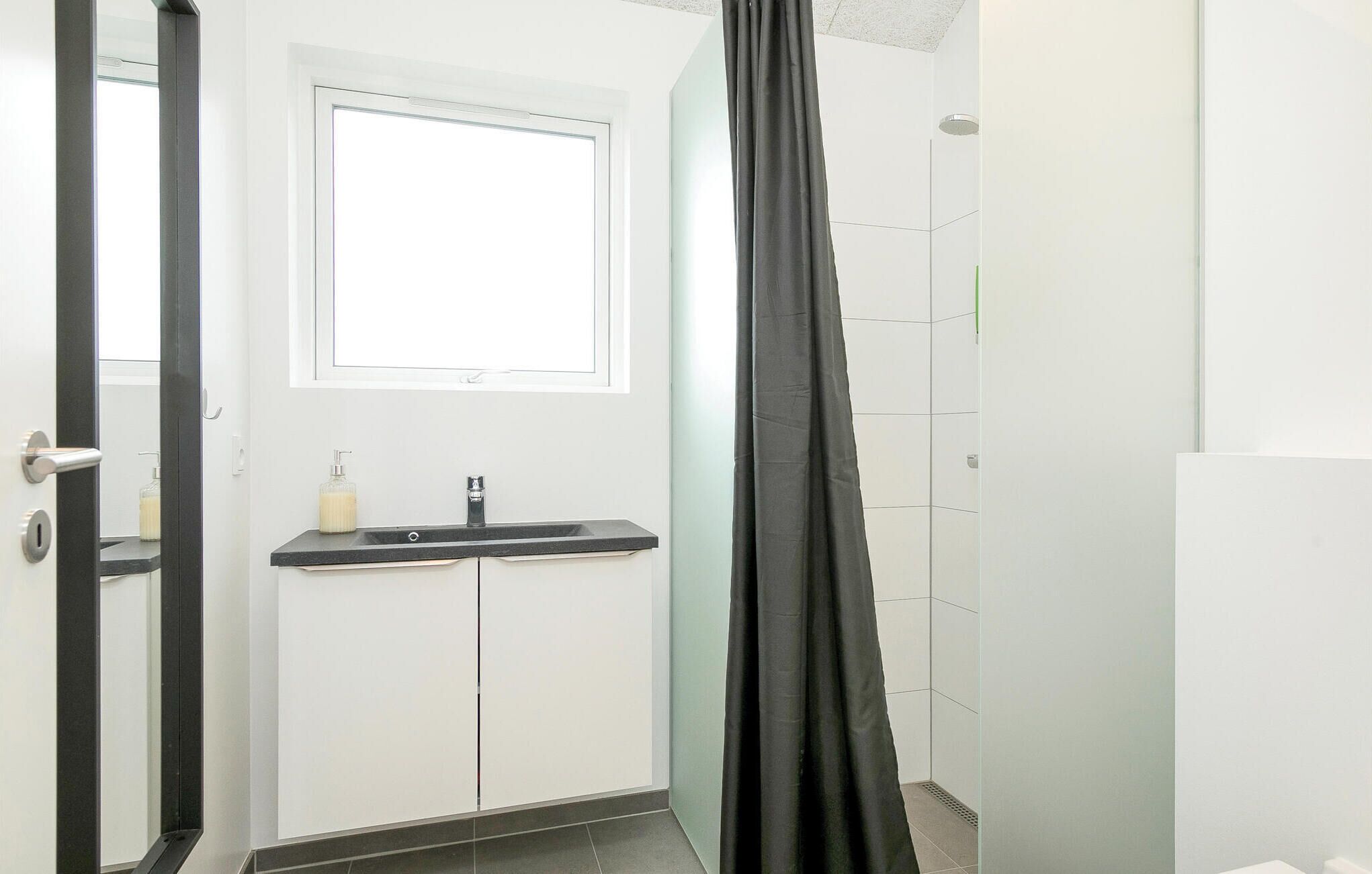 Une salle de bain avec un lavabo blanc, un miroir, une fenêtre et un rideau de douche.