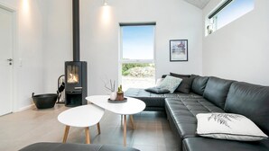 A modern living room with a black leather sofa, a white coffee table, and a black wood-burning stove.