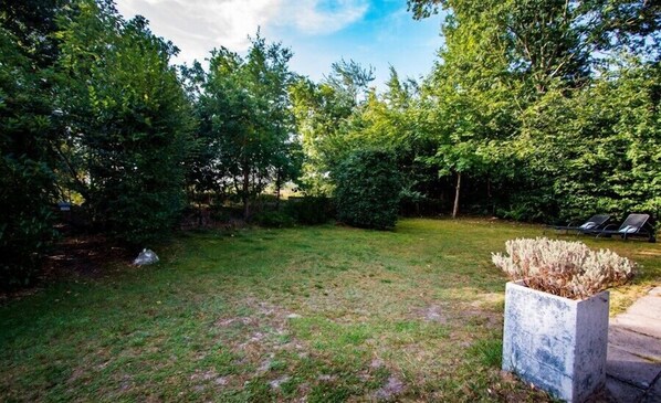 A grassy backyard with a stone planter and a row of chairs. - Populierenlaan 13 bungalow on holiday location with beautiful view (Nieuw-Haamstede)