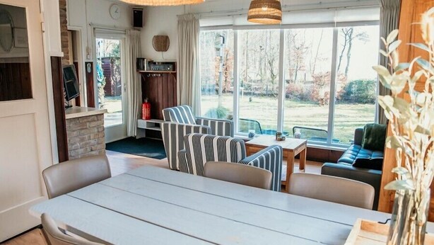 Un salon chaleureux avec une table à manger, des chaises à rayures, un canapé et une grande fenêtre donnant sur l’extérieur.
