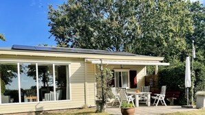 Une maison de plain-pied dotée de grandes fenêtres, d’un patio avec des meubles d’extérieur et d’un panneau solaire sur le toit.