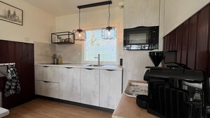 Une cuisine compacte dotée d’un four à micro-ondes encastré, d’un luminaire suspendu et d’une fenêtre avec des stores.