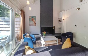 A modern living room with a fireplace, blue sofas, a coffee table, and a large window with curtains. - Amazing home in Bruinisse with kitchen (Bruinisse)