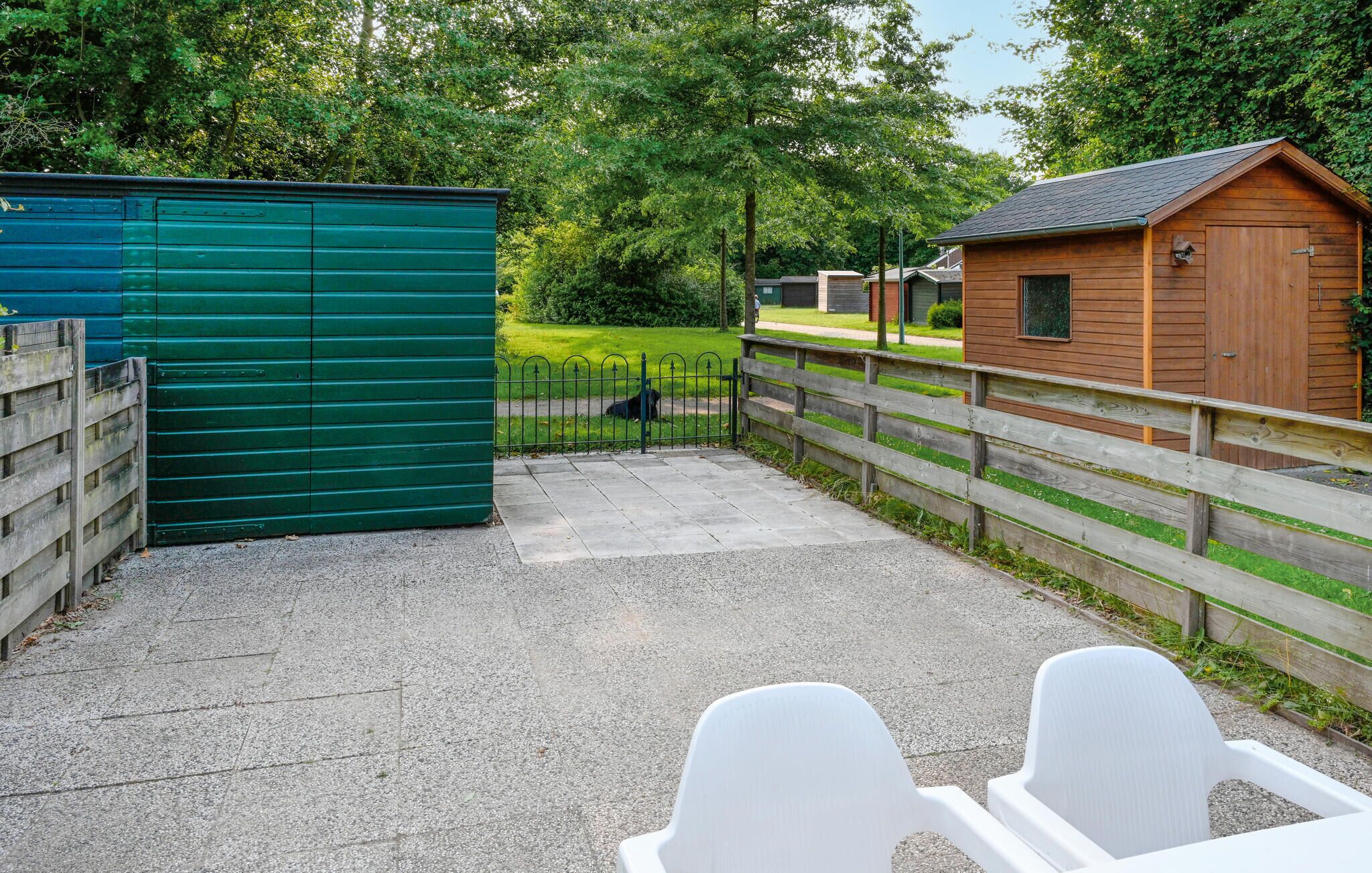 A fenced outdoor area with a green shed, a wooden building, and a paved path.