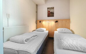 A small, single-room accommodation with two single beds, a wooden headboard, a radiator, and a wall-mounted light fixture. - Amazing home in Bruinisse with kitchen (Bruinisse)