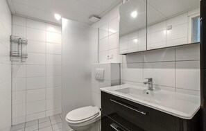 A modern bathroom with white tiles, a toilet, a sink with a mirror, and a shower area. - Amazing home in Bruinisse with kitchen (Bruinisse)
