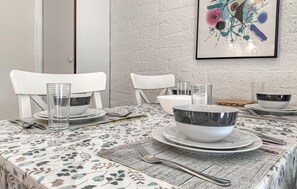 A dining table set with white chairs, clear glasses, and metal bowls on a patterned tablecloth.