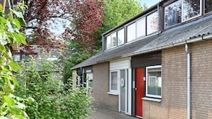 A two-story building with a red door, a small garden area, and a view of a neighboring building. - Amazing home in Bruinisse with kitchen (Bruinisse)