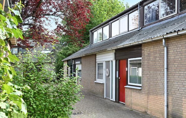 A two-story building with a red door, a small garden area, and a view of a neighboring building. - Amazing home in Bruinisse with kitchen (Bruinisse)