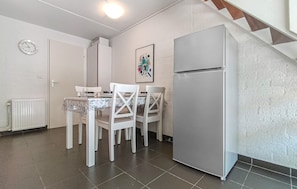Une cuisine compacte avec des meubles blancs, un réfrigérateur, une table à manger avec des chaises et une seule horloge murale.