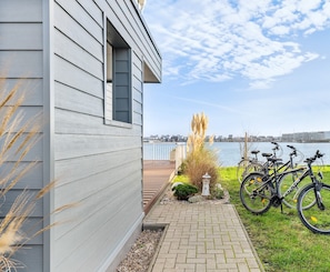 A house with a view of a body of water, a paved pathway, and bicycles parked outside. - Light-flooded villa with large terrace, direct waterfront, wellness area (Kappeln)