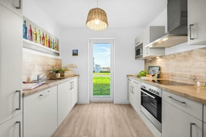 Una cocina moderna con armarios blancos, encimera de madera, horno de acero inoxidable y un ventanal amplio.