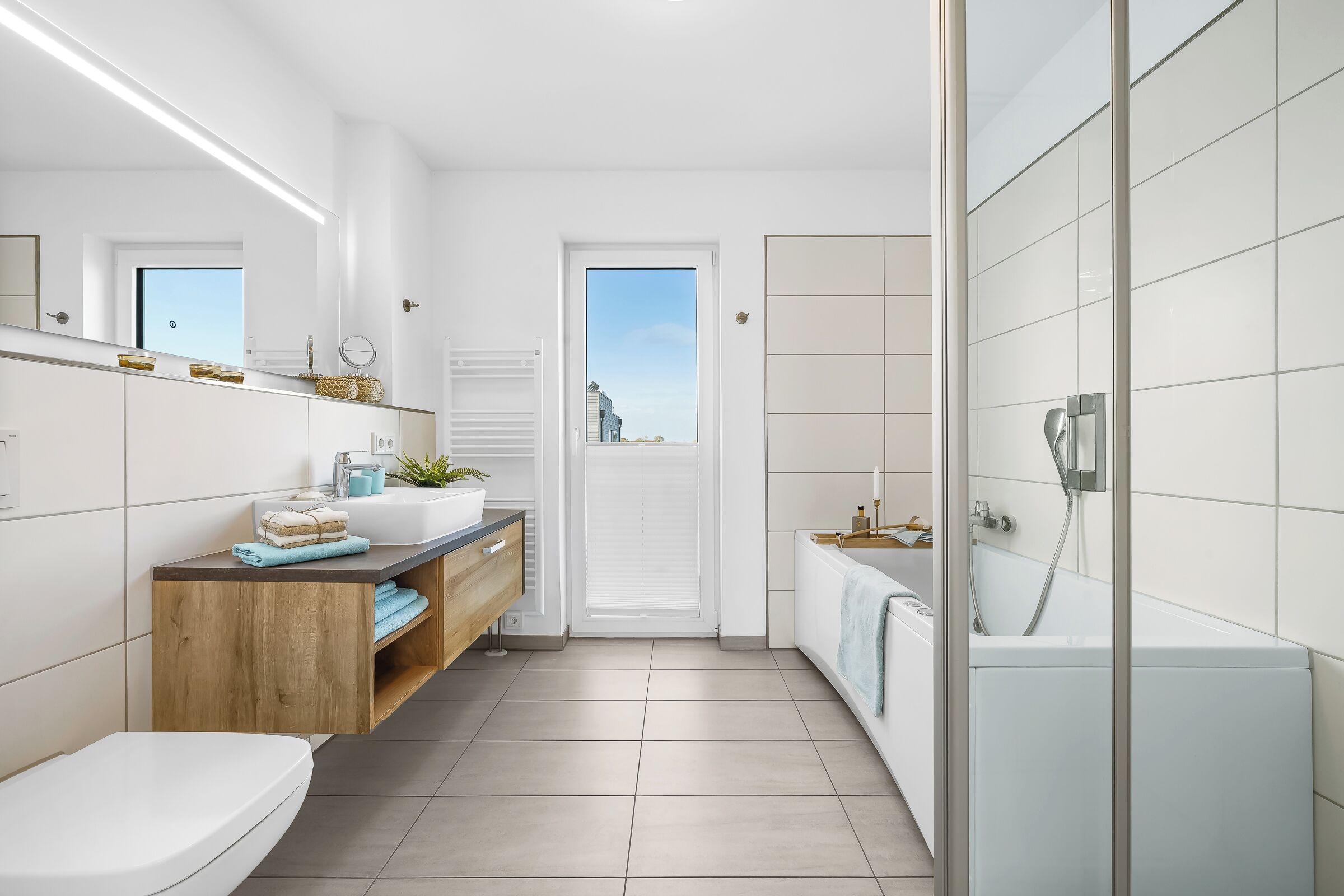 Un baño moderno con inodoro, lavamanos y zona de ducha, que incluye un mueble de tocador de madera y vistas a través de la puerta.