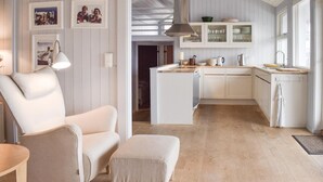 Une cuisine moderne avec des meubles blancs, un four encastré et un plan de travail en bois. On y trouve également un coin repas avec une chaise blanche et une petite table.