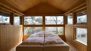 Une pièce de style cabane en bois, avec un lit, de grandes fenêtres et un plafond en pente.
