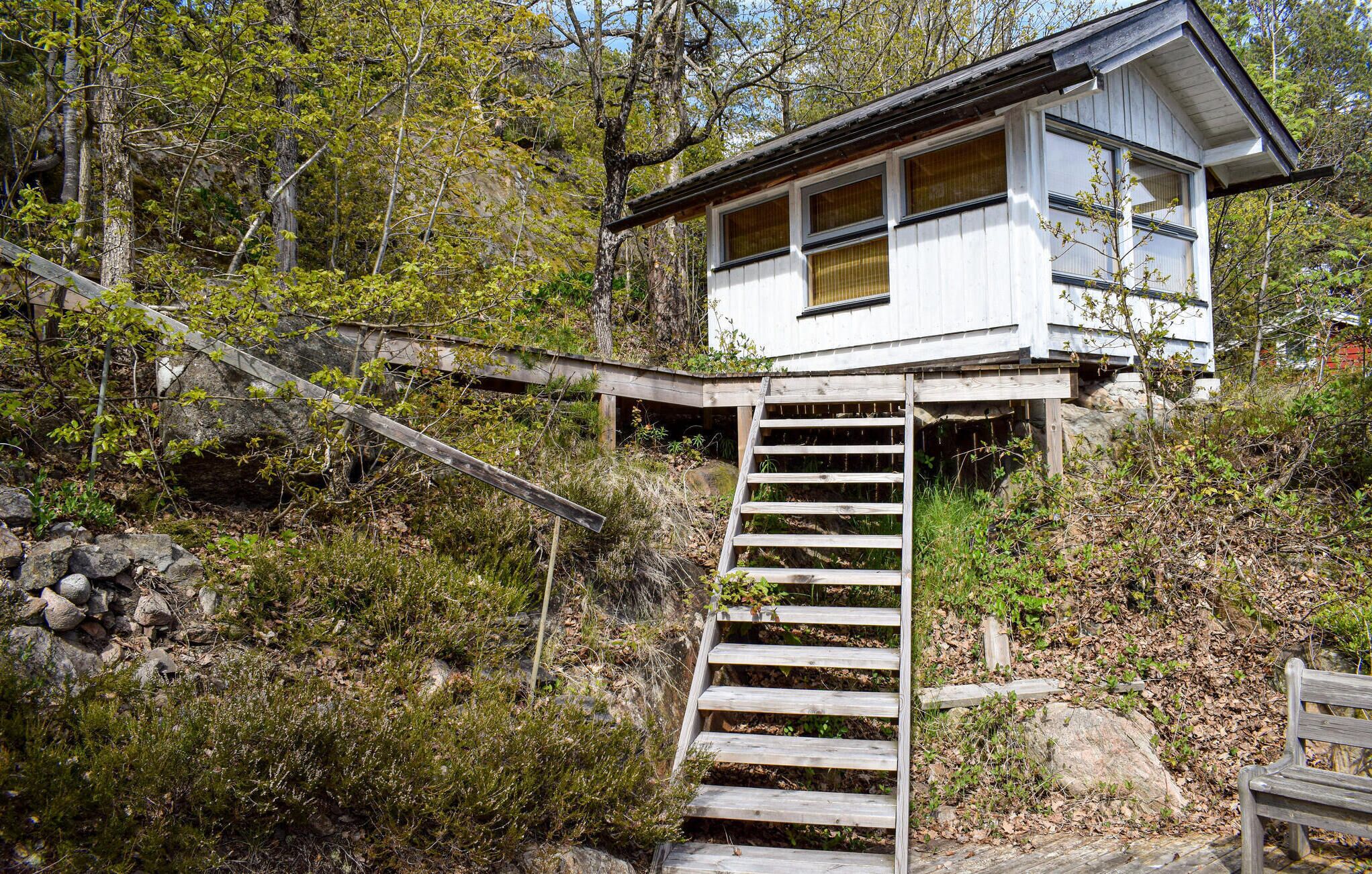 A cabin with a wooden staircase leading up to it, surrounded by trees and vegetation.