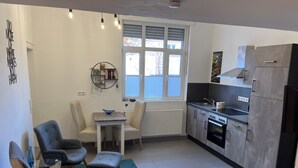 A modern kitchen with a dining area, featuring a table and chairs, a built-in oven, and a window with blinds. - Dalhaus farm: Our "pantry" (Lüdinghausen)