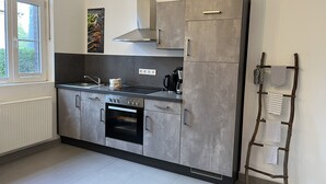 A modern kitchen with grey cabinets, a stainless steel range hood, and a built-in oven. There is a window providing natural light and a wall-mounted rack with towels. - Dalhaus farm: Our "pantry" (Lüdinghausen)