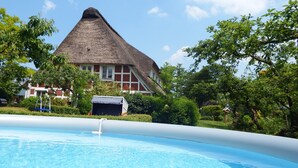 Una casa con techo de paja, piscina y follaje circundante.