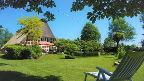 A house with a thatched roof, surrounded by a well-maintained lawn and various trees. - Family house, Villa Country house, 10 pers, 
3 apartments, 3 bathroom, 3 kitchen (Hemmoor)