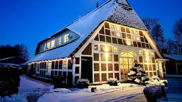 Un edificio cubierto de nieve con ventanas amplias y un techo pronunciado, iluminado por luces interiores.