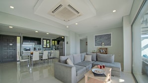 A modern living room with a grey sofa, a wooden coffee table, and a dining area with white chairs.