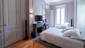 Ein Schlafzimmer mit einem großen Bett, einem Kamin, einem Fernseher und Blick ins Freie durch ein Fenster.