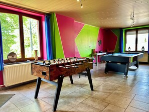 Ein Zimmer mit Tischfußball, Billardtisch und einem Fenster mit Vorhängen.