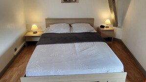 A bedroom with a wooden bed, two bedside tables with lamps, a wooden headboard, and a small picture on the wall.