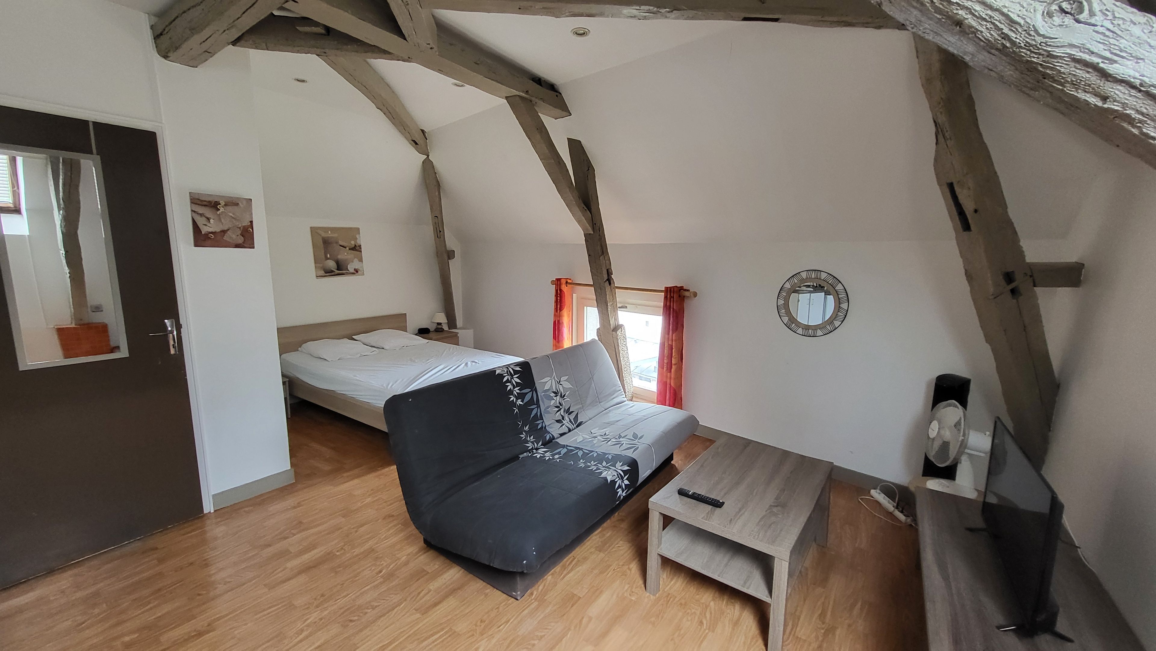 Une chambre à coucher avec un lit, un canapé, une petite table, un miroir et un ventilateur.