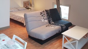 A cozy loft bedroom with a bed, a sofa, a small table, and a window. - Studio 7 - 3 min from Futuroscope - 1 to 4 persons (Chasseneuil-du-Poitou)