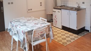 A compact kitchen with a sink, stove, and white cabinets. There is a dining table with chairs and a clock on the wall. - Studio 7 - 3 min from Futuroscope - 1 to 4 persons (Chasseneuil-du-Poitou)