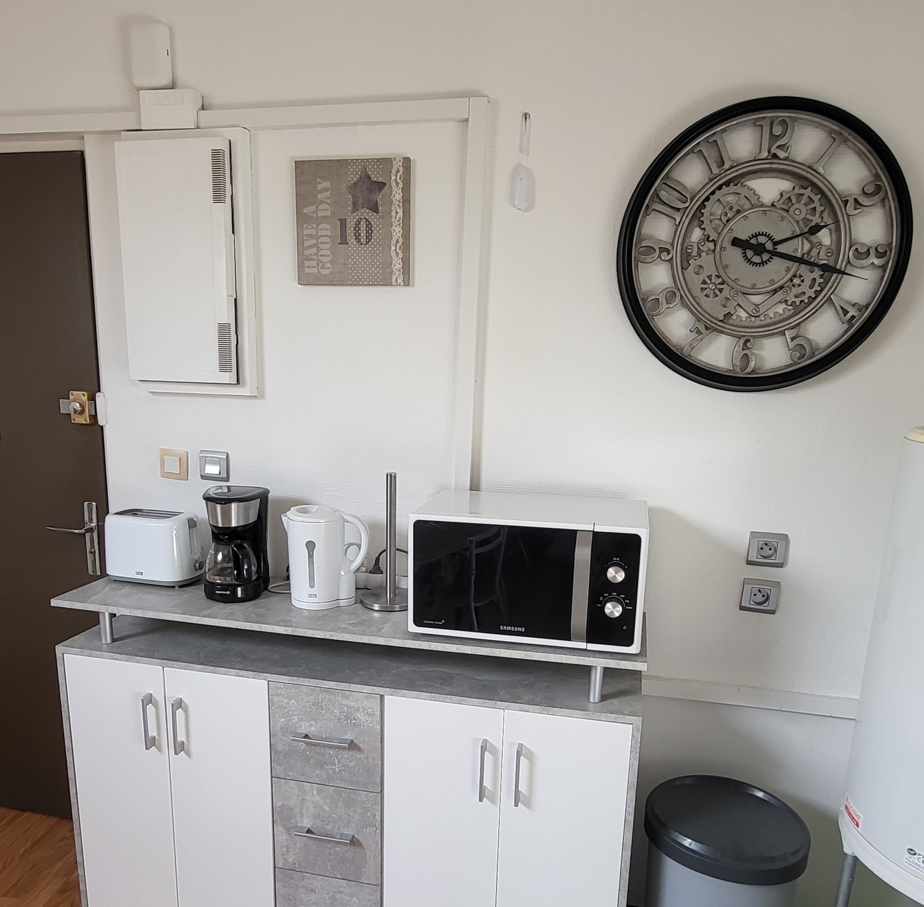 A kitchenette with a microwave, toaster, coffee maker, and a clock on the wall.