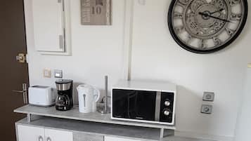 A kitchenette with a microwave, toaster, coffee maker, and a clock on the wall.