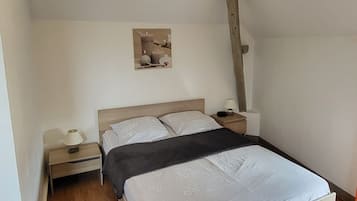 Een slaapkamer met een houten bed, nachtkastje, wandlamp en een plafond met zichtbare balken.