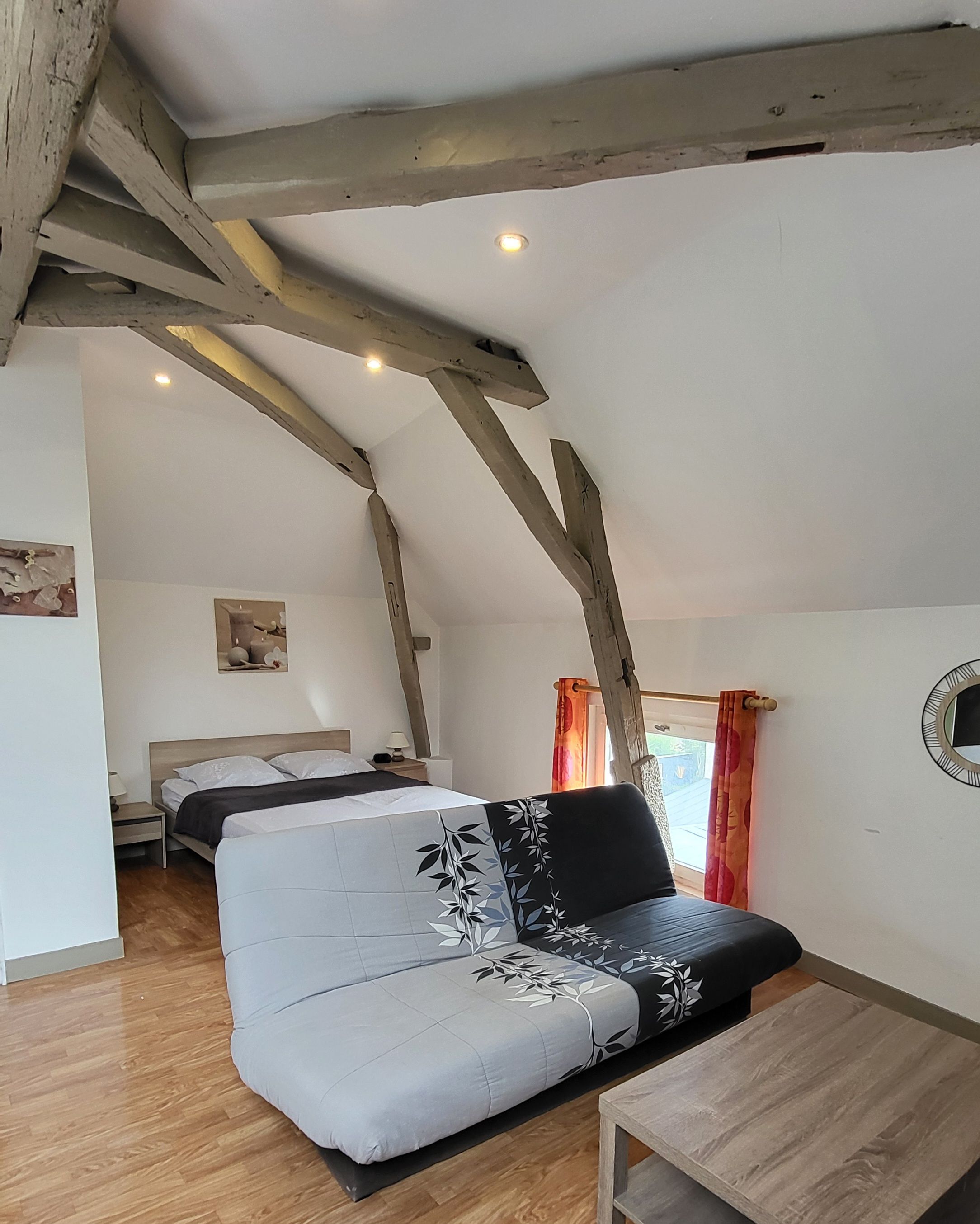 A room with a sofa, a bed, wooden beams, a small table, and a picture on the wall.
