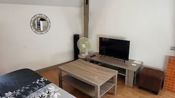 A living room with a sofa, a TV, a fan, and a wooden coffee table.