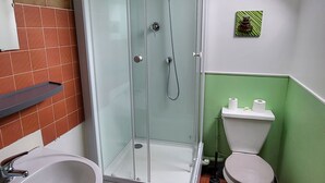 A bathroom with a glass-enclosed shower, a sink, a toilet, and a small shelf.