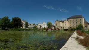 A serene riverside scene with buildings, a clear sky, and a calm water surface with lily pads. - Studio 7 - 3 min from Futuroscope - 1 to 4 persons (Chasseneuil-du-Poitou)