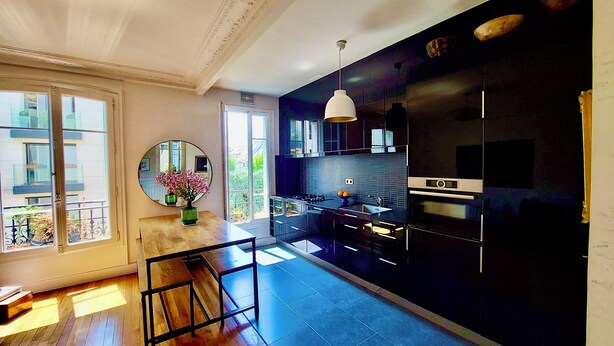 A modern kitchen with a large window, a round mirror, and a wooden dining table.