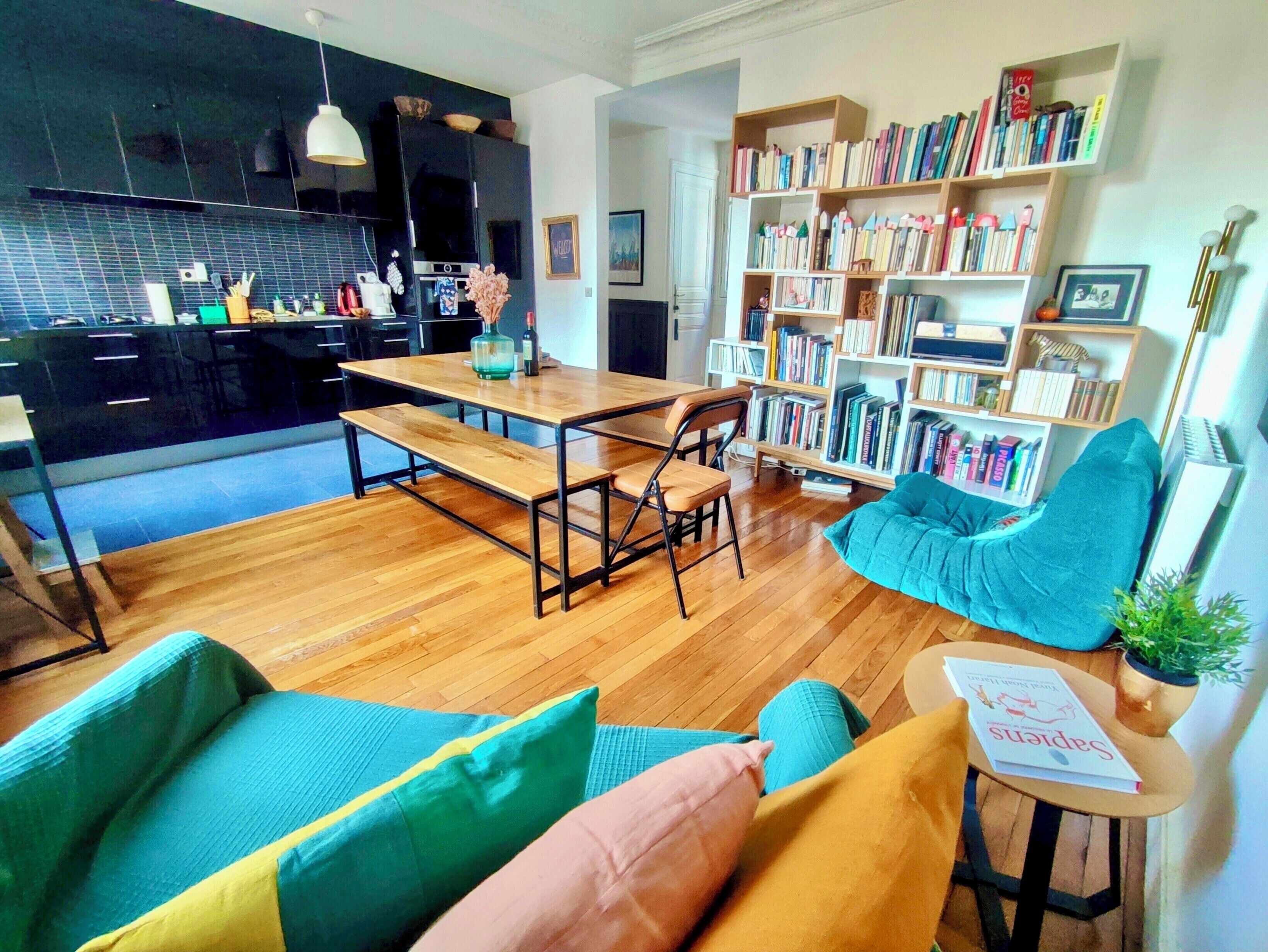 Una sala de estar moderna con una mesa de comedor de madera, una estantería y un rincón de estar acogedor con cojines.