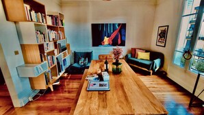 A living room with a wooden table, bookshelves, a sofa, and a painting on the wall.