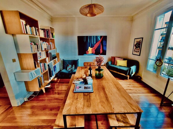 Un salon avec une table en bois, des étagères, un canapé et un tableau accroché au mur.