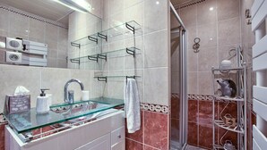 Une salle de bain avec un lavabo en verre, un porte-serviettes, un espace douche et une étagère contenant des articles de toilette.