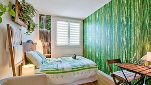 Une chambre à coucher comprenant un lit, une chaise, une table et un mur recouvert d’un papier peint à motifs de bambou vert.