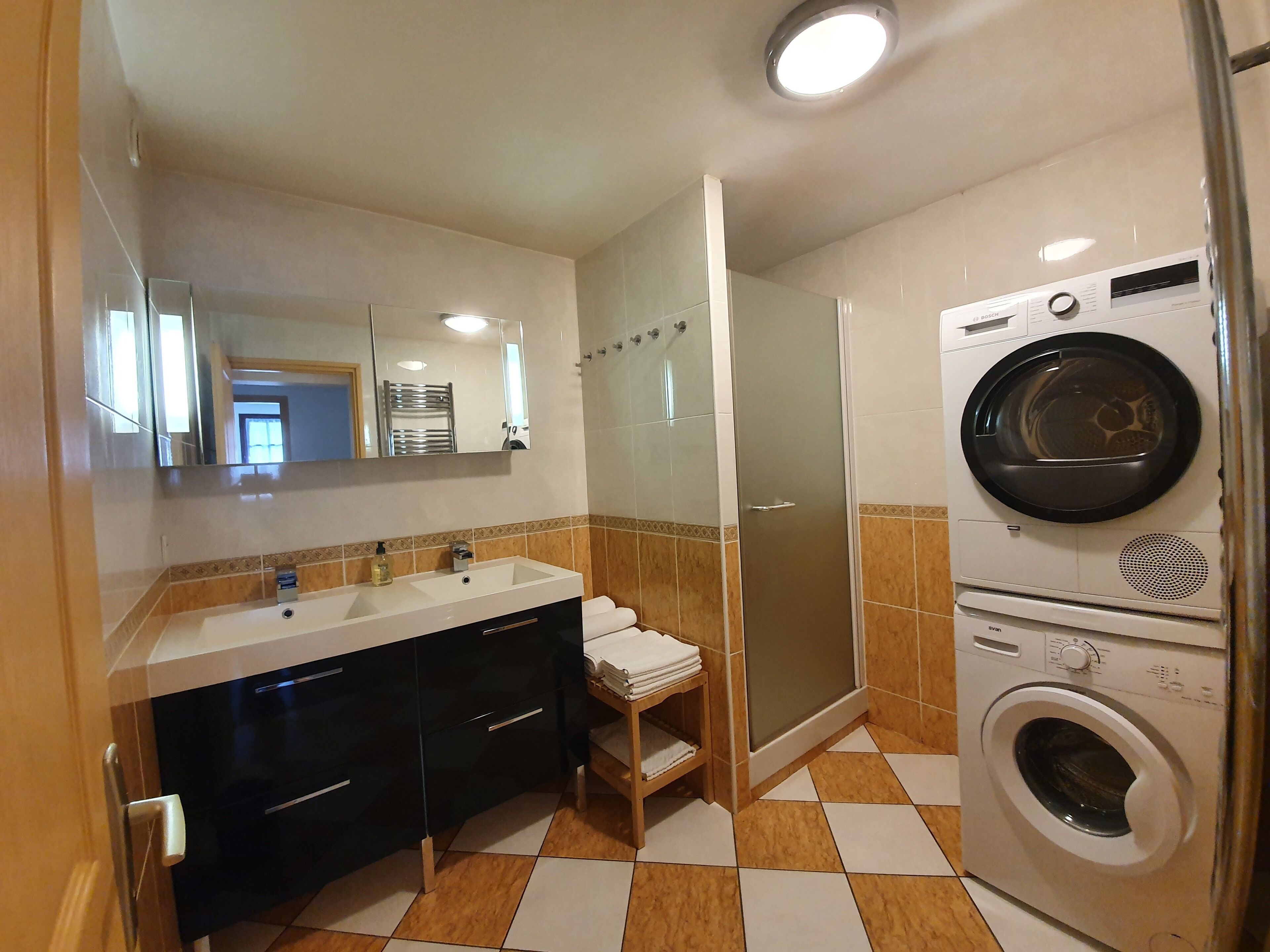 Ein Badezimmer mit Waschbecken, Spiegel, Handtuchhalter, Dusche und einer Waschmaschine.
