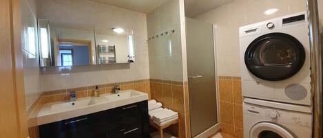Ein Badezimmer mit Waschbecken, Spiegel, Handtuchhalter, Dusche und einer Waschmaschine.