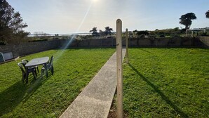 Un área verde exterior con un sendero de concreto, una mesa con sillas y vista al mar.